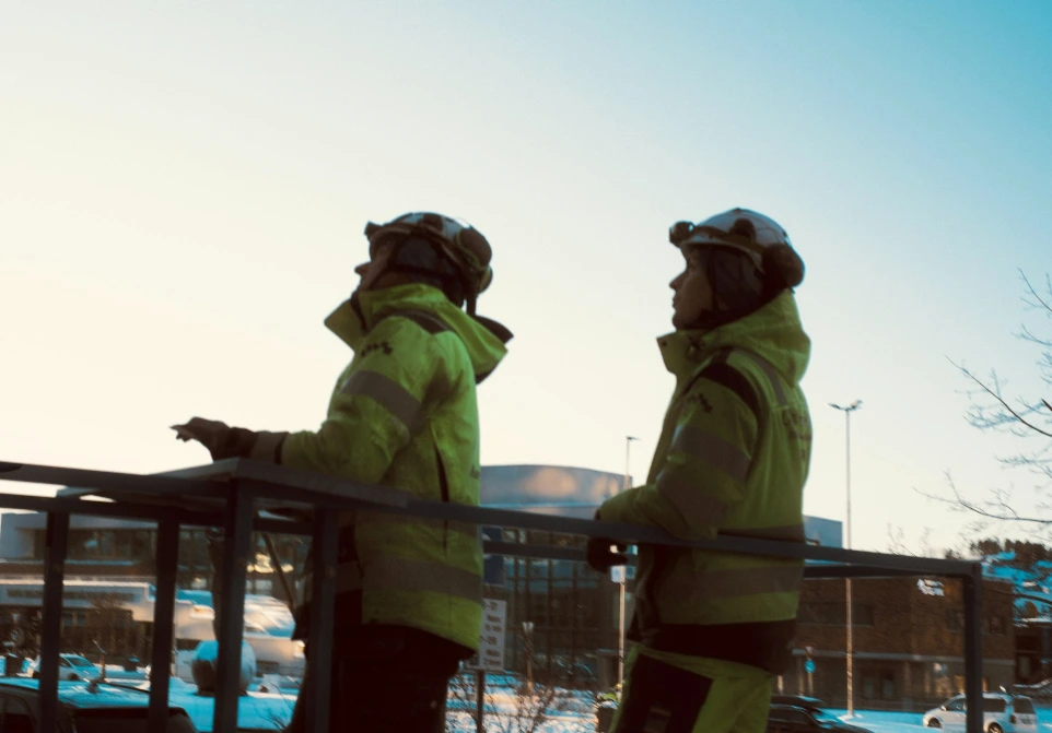Two people in high-visibility jackets looking up